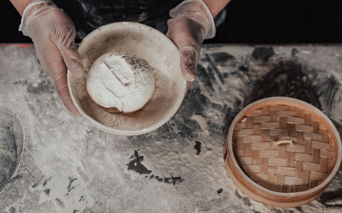 Hands working flour and dough in a bowl during bread preparation.