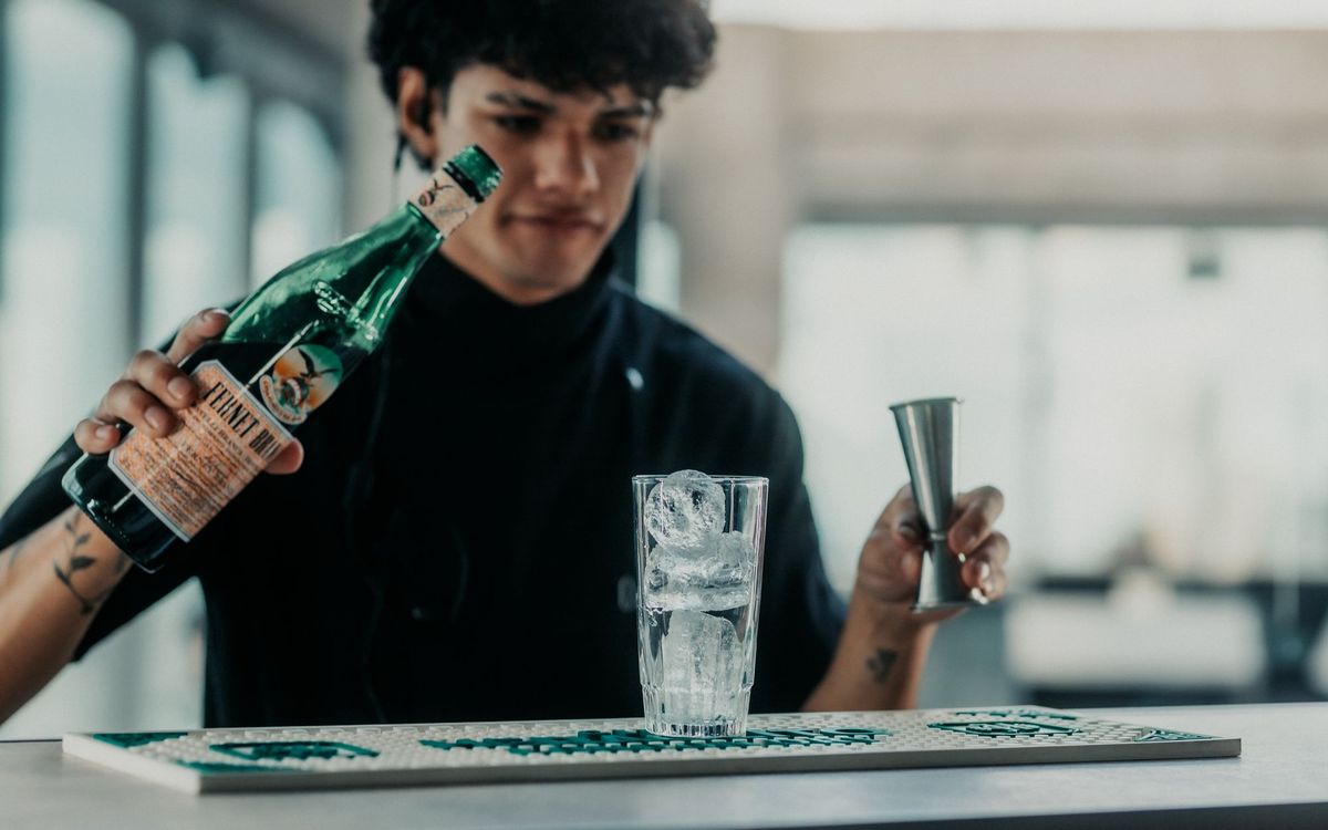 Bartender pouring a drink into a glass with ice at a bar.