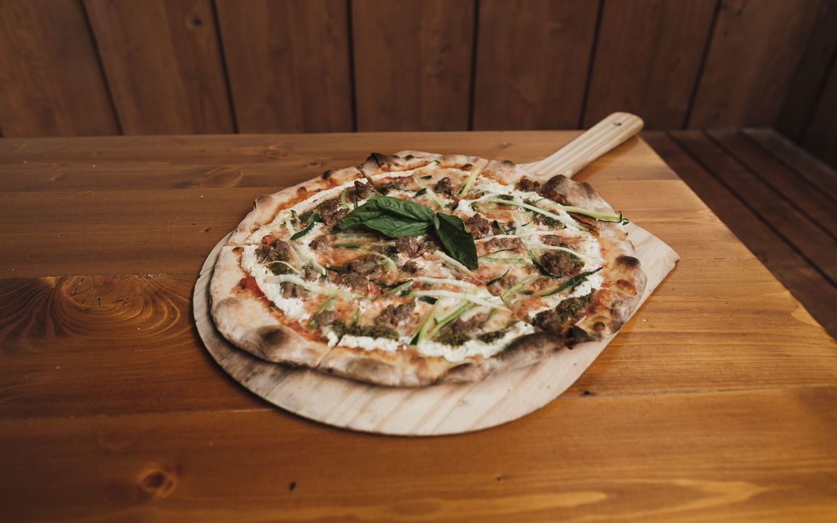 A pizza with basil and cheese, baked until the crust is charred, resting on a wooden peel.