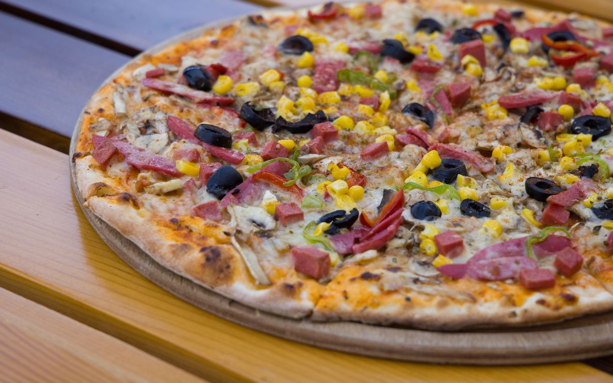 Close-up of a mouthwatering pizza with various toppings on a wooden table outdoors