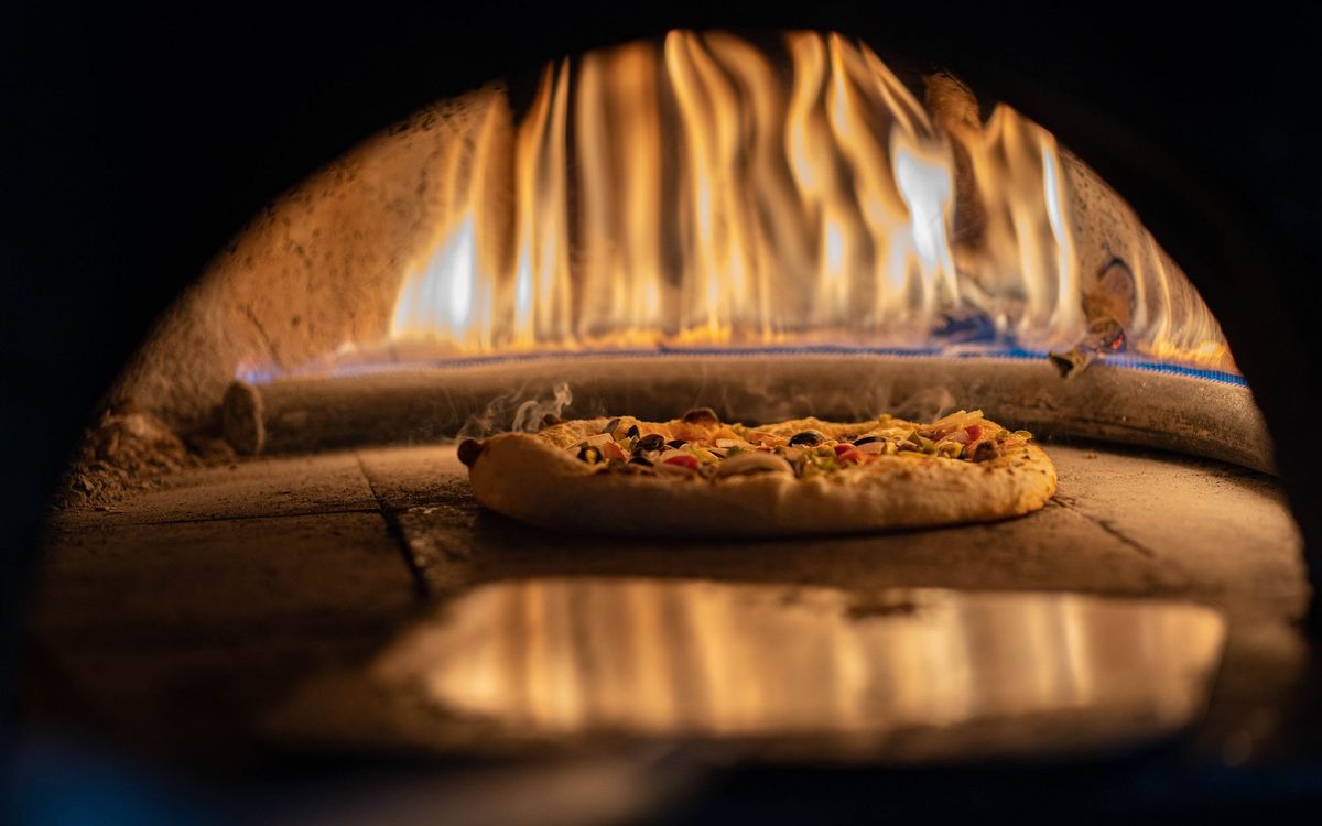 Pizza baking on the stone of a gas pizza oven with a rolling flame at the back