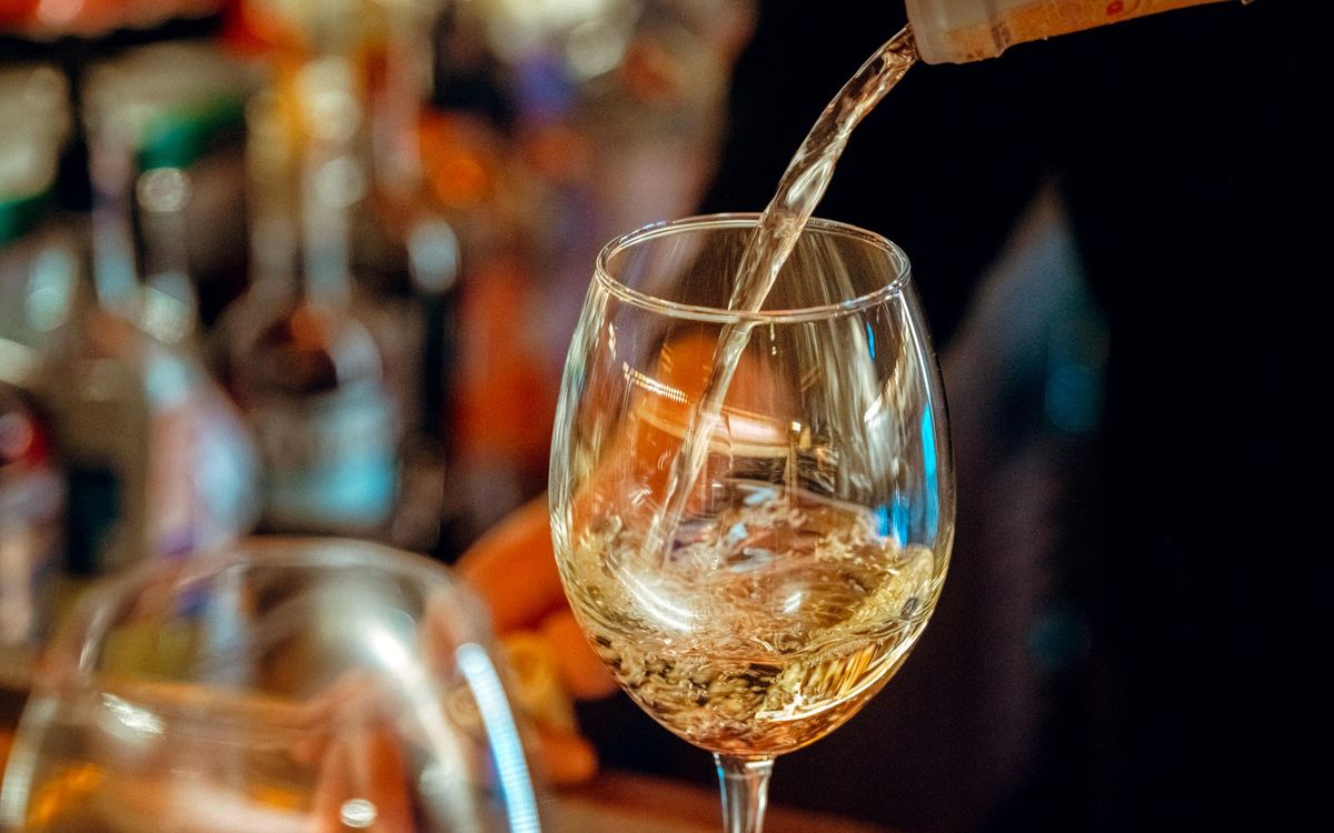 A close-up of white wine being poured into a glass, the serving temperature a wine cooler protects