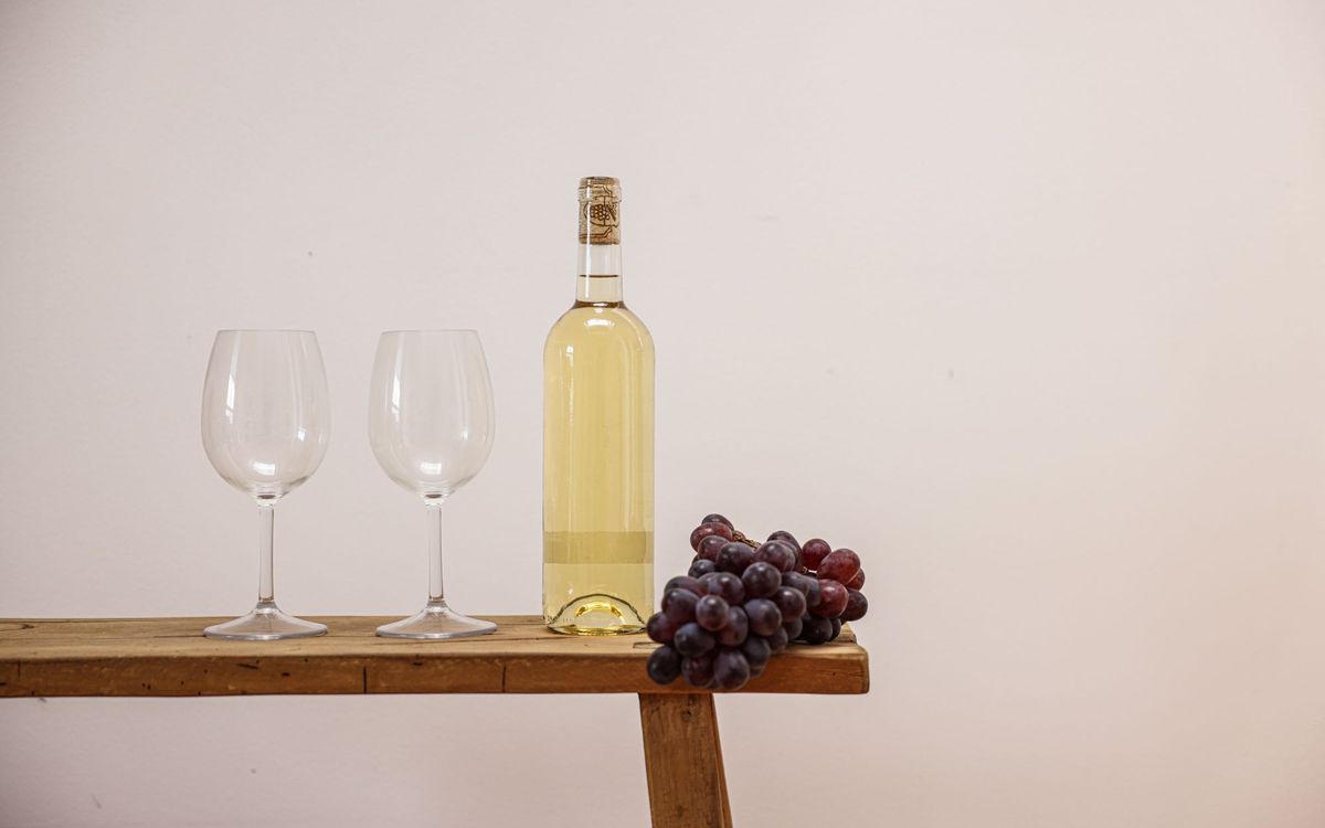 Minimalist still life image featuring wine bottle, two glasses, and grapes on wooden table