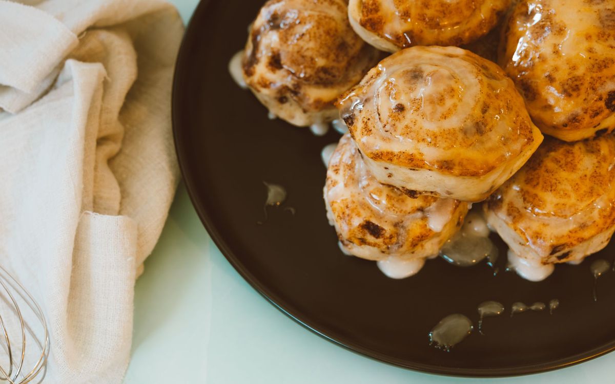 Close-up view of freshly baked cinnamon rolls drizzled with icing on a black plate