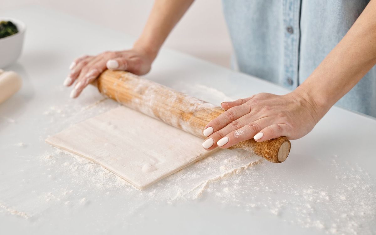 Hands rolling pastry dough on a floured surface with a wooden pin