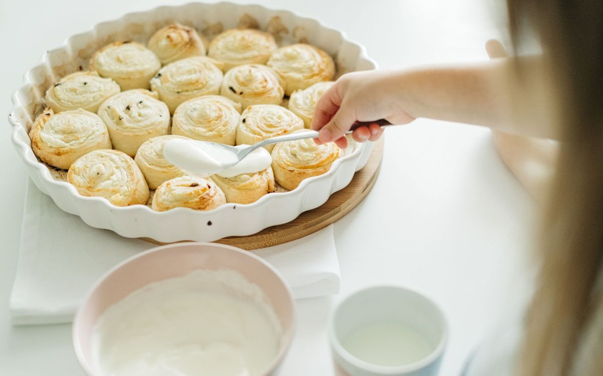 A child spreads creamy icing over freshly baked cinnamon rolls