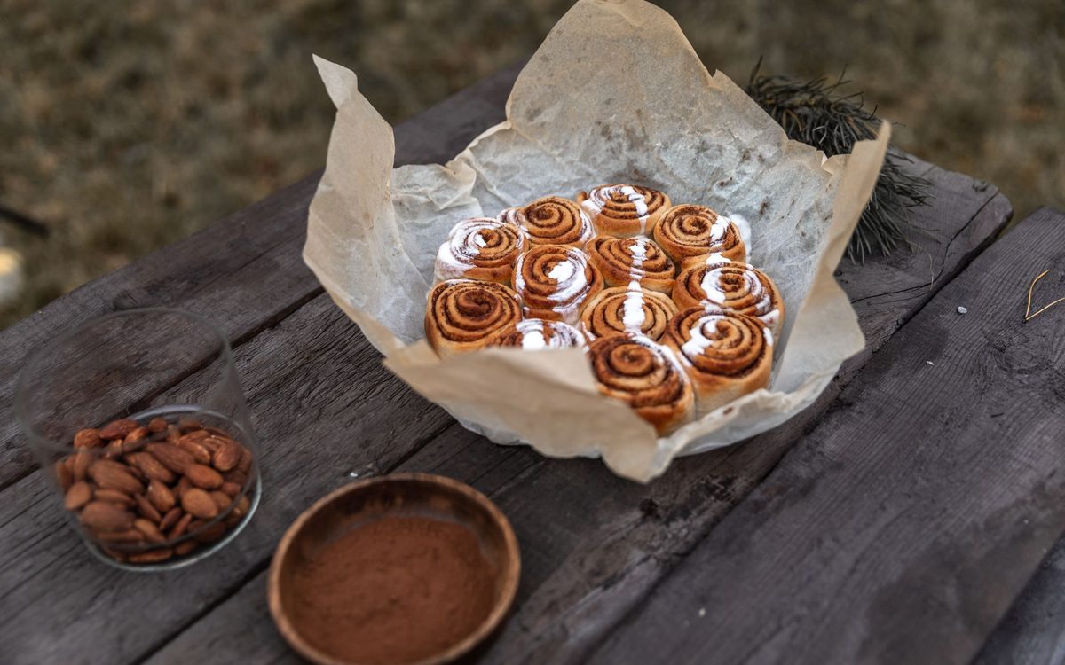 Freshly baked cinnamon rolls on parchment paper on a wooden table with almonds and cinnamon