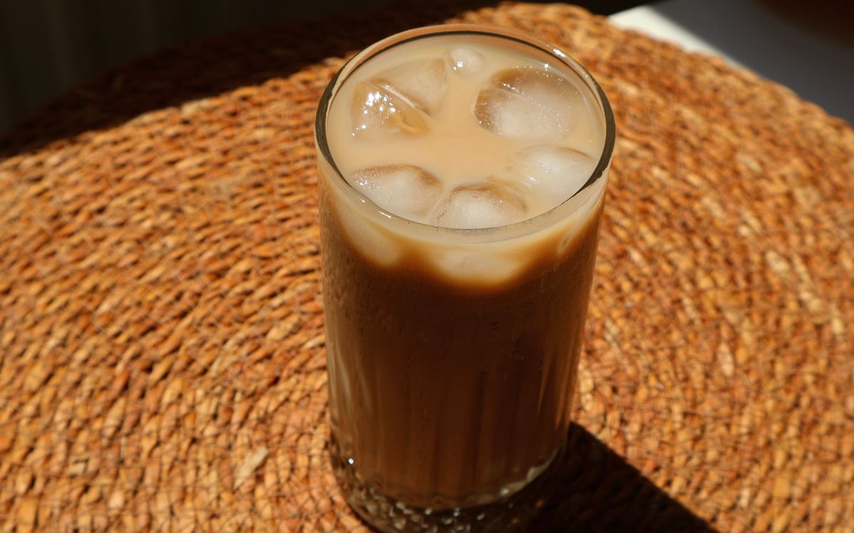 Glass of iced coffee with ice cubes on a woven mat in sunlight