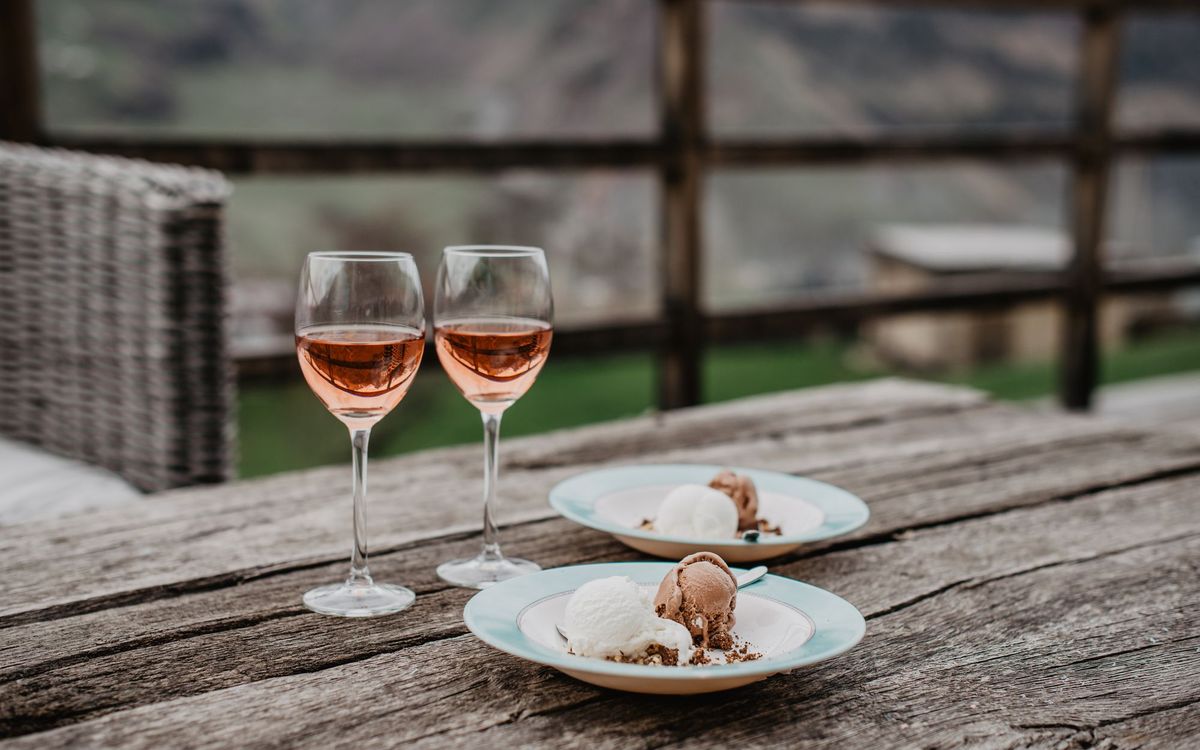 Rustic wooden outdoor table with two glasses of rosé wine and dessert plates featuring chocolate and vanilla ice cream