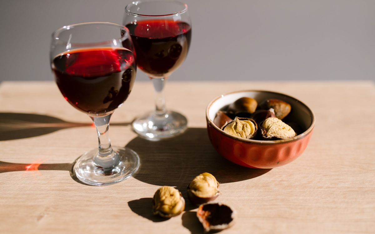Two glasses of red wine with a bowl of roasted chestnuts on a wooden table under natural light