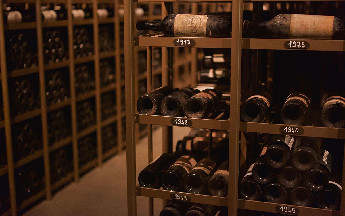 Old dusty wine bottles lying on metal racks labeled with vintage years in a dark cellar, the steady cool storage a wine fridge copies at home.