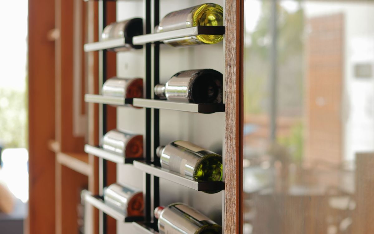 Wine bottles lying on their sides on slim metal shelves in a wooden frame in daylight, an example of storing bottles horizontally.