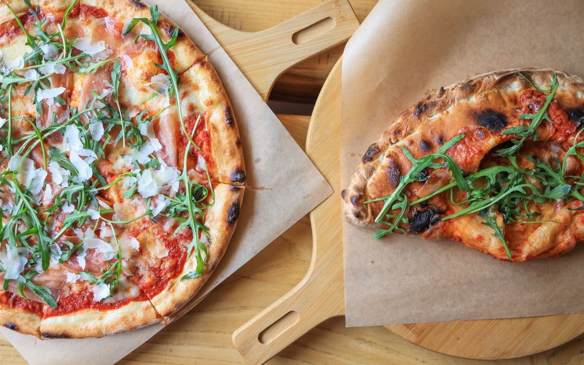 Two baked pizzas with arugula and a charred crust on wooden boards