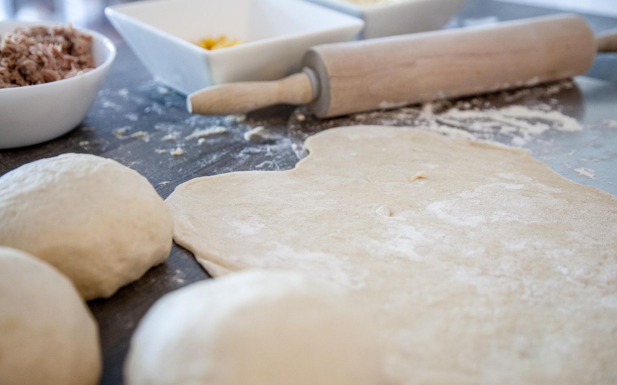 Flour-dusted dough balls and rolled-out dough beside a rolling pin on a dark counter