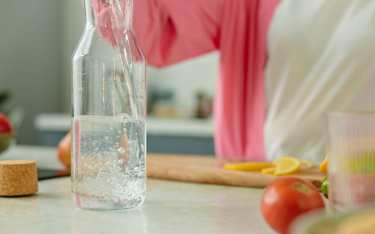 Water pouring into a glass carafe on a kitchen counter, the kind of clean water you need for rinsing an ice maker
