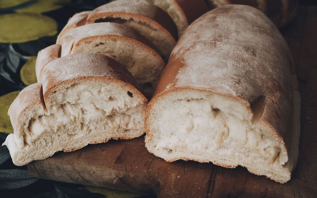 Rustic white loaf with a floury crust, partly sliced on a wooden board.