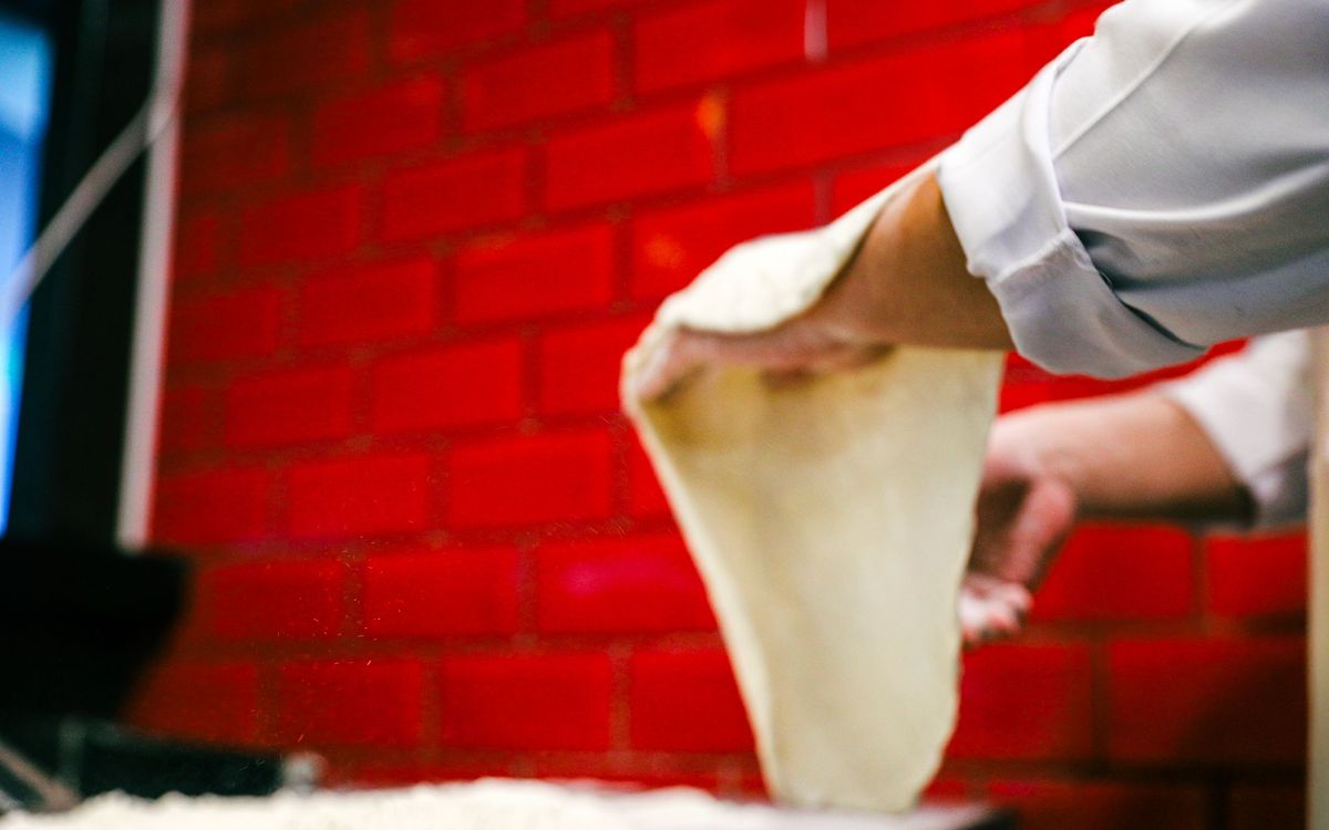 Chef skillfully stretches pizza dough in a vibrant kitchen with red brick walls.