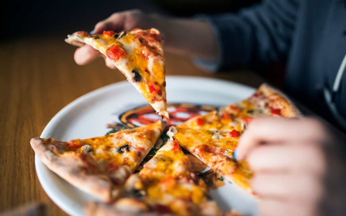A hand lifting a cheesy pizza slice with peppers and mushrooms from a plate of slices