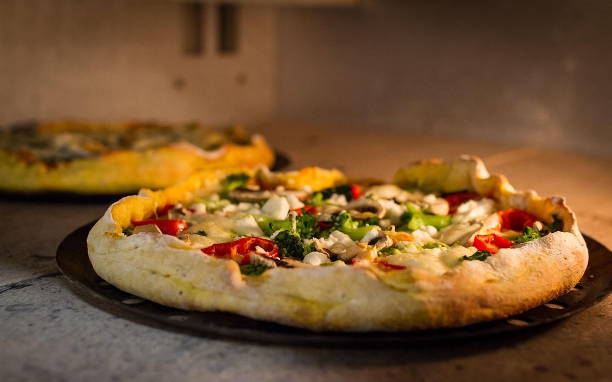 A baked vegetable pizza on a dark round pan inside a lit oven