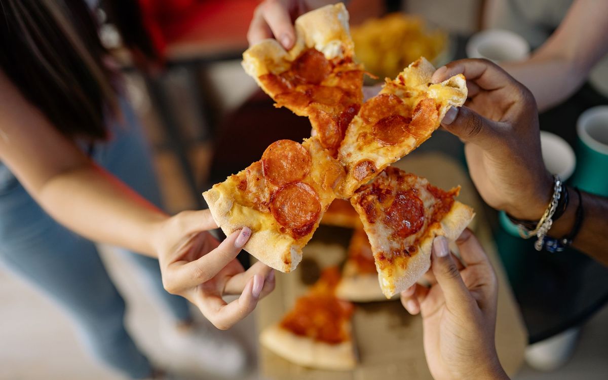 Hands from several people each holding a pepperoni pizza slice together over a table