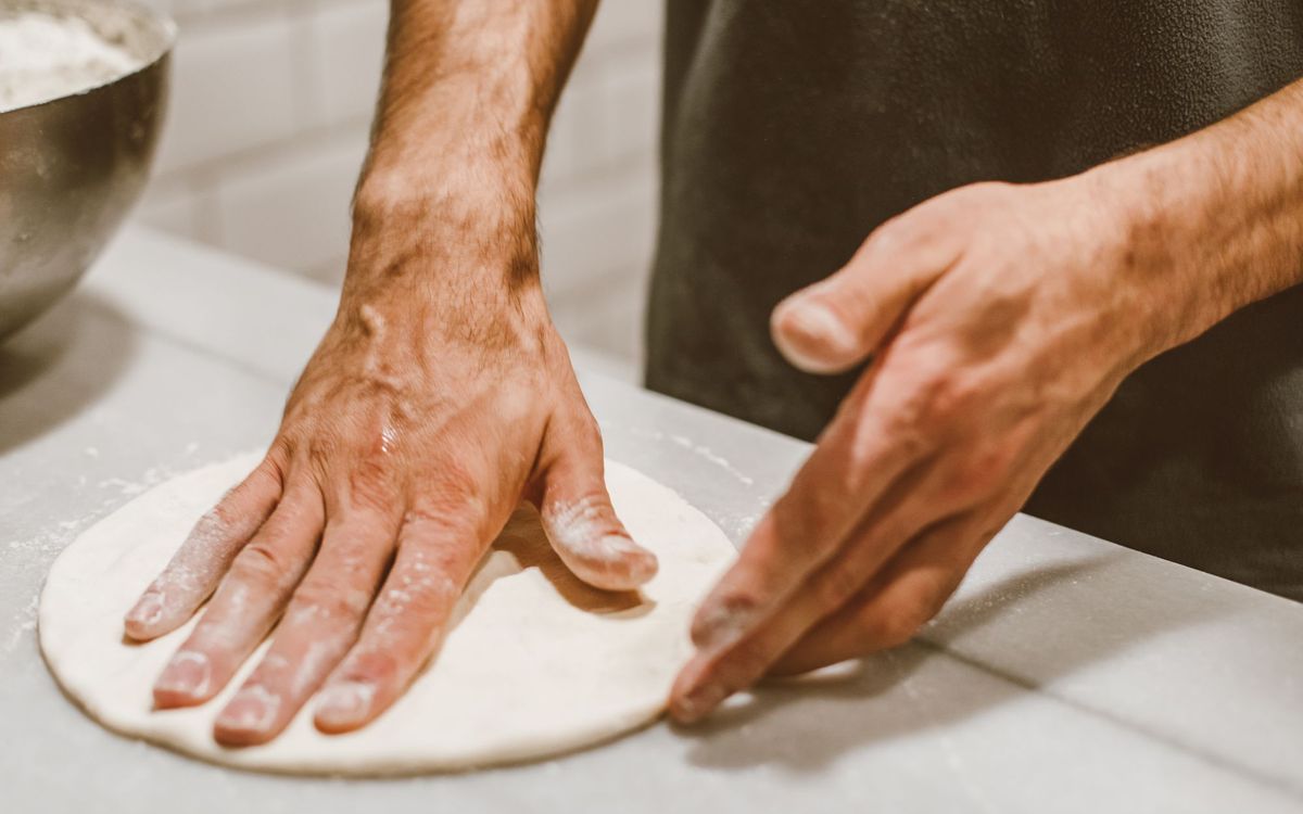 Close-up of hands shaping pizza dough on a floured counter