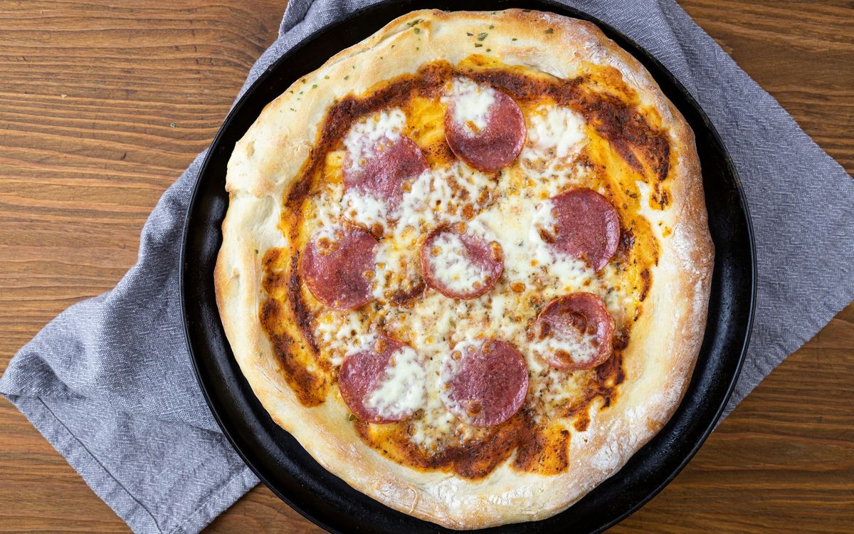 Close-up of a homemade pepperoni pizza with melted cheese and a browned crust on a rustic wooden table