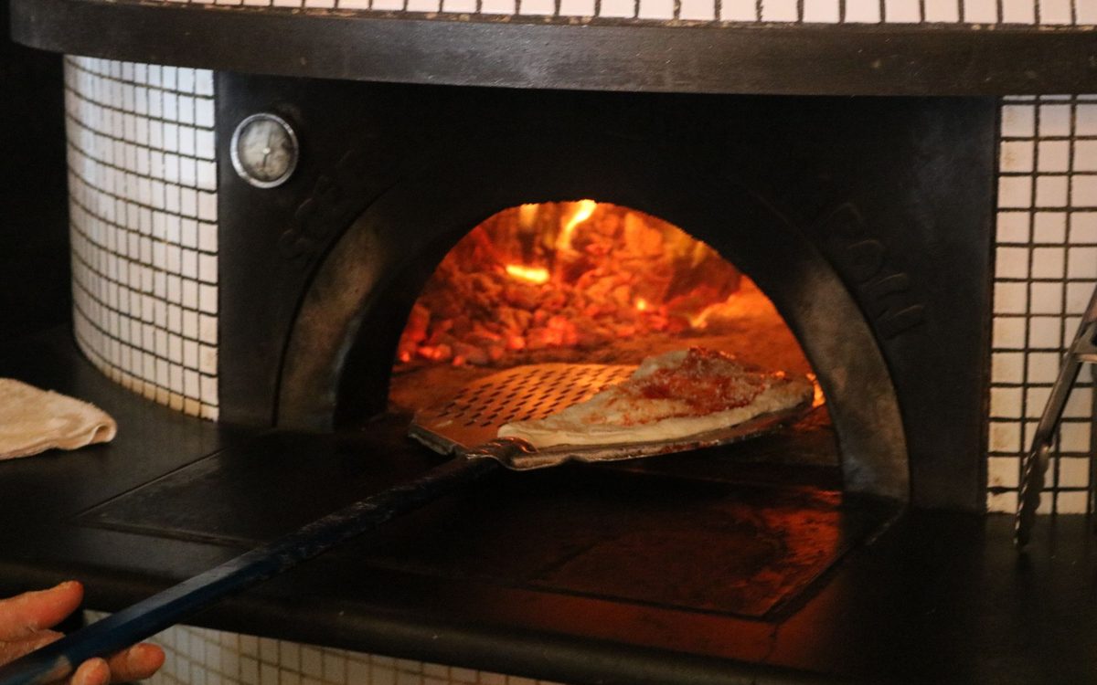 Close-up of a pizza being baked in a traditional wood-fired oven, showcasing culinary authenticity