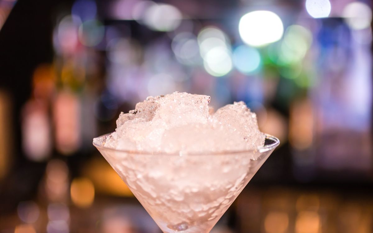 Elegant cocktail glass filled with crushed ice, highlighted by colorful bokeh lights in a nightclub setting.