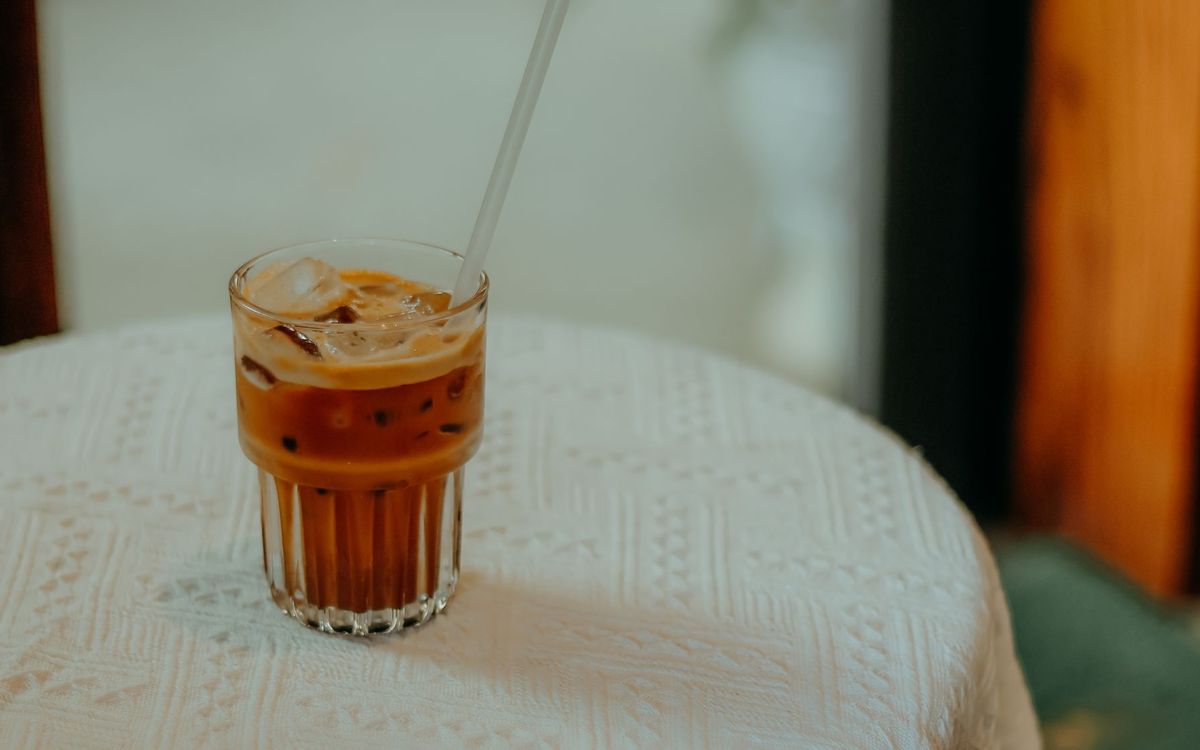 Glass of iced coffee with a straw on a lace-covered table.