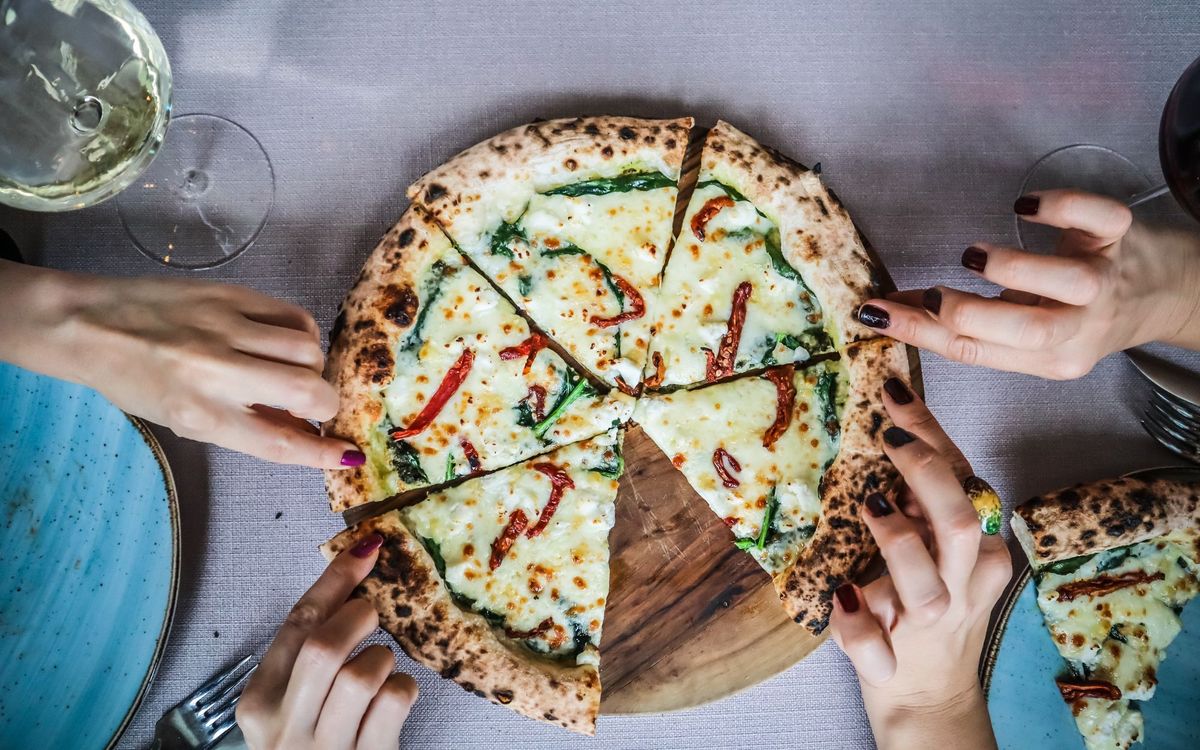 Close-up of hands grabbing gourmet pizza slices, paired with wine in a casual dining setting