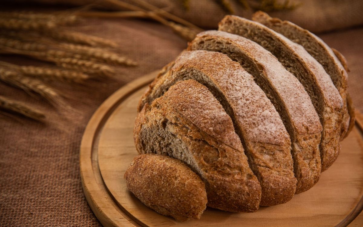 Artistic shot of sliced whole wheat bread on a round wooden board with wheat stalks.