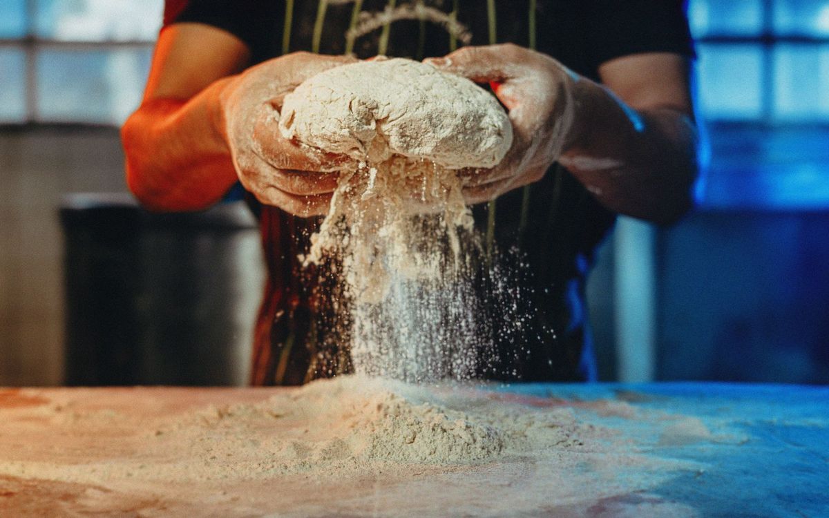 A baker works by hand with flour and dough, creating artisanal bread in an industrial kitchen setting.