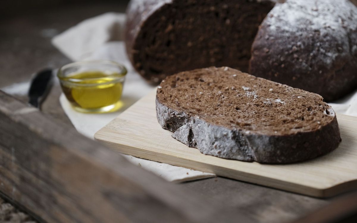 A slice of fresh whole grain bread on a wooden board accompanied by olive oil, perfect for a healthy breakfast.
