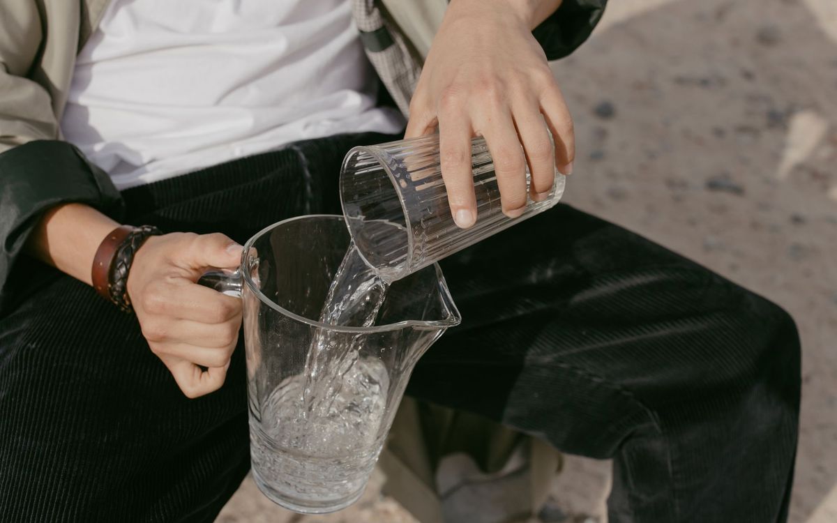 Close-up of a person pouring fresh water from a glass into a pitcher.