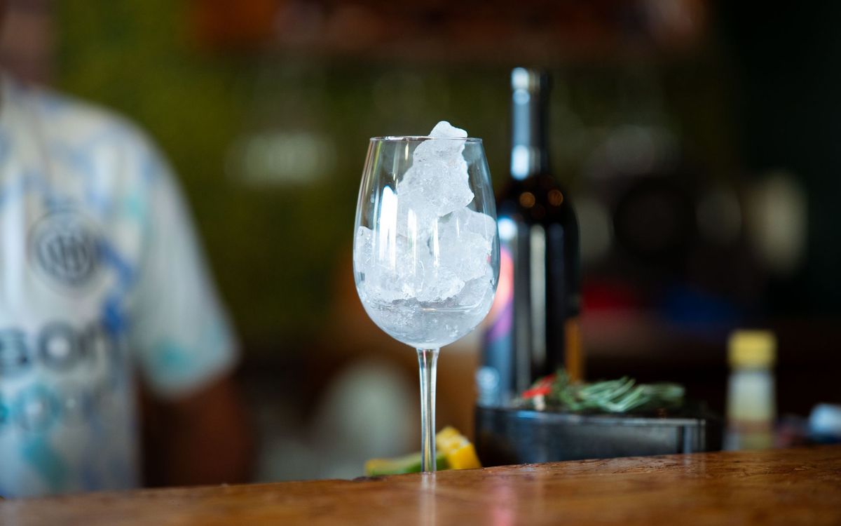 Glass with ice on a bar counter, next to a bottle.
