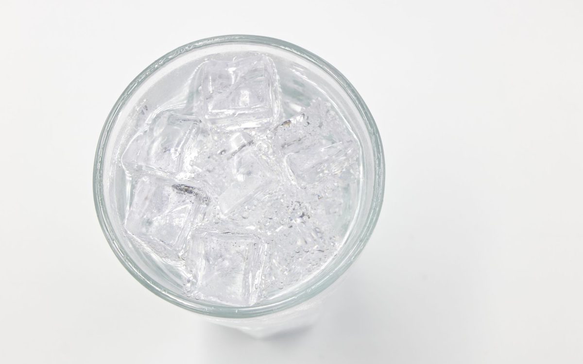 Top-down view of a clear glass filled with ice cubes and water on a white background.