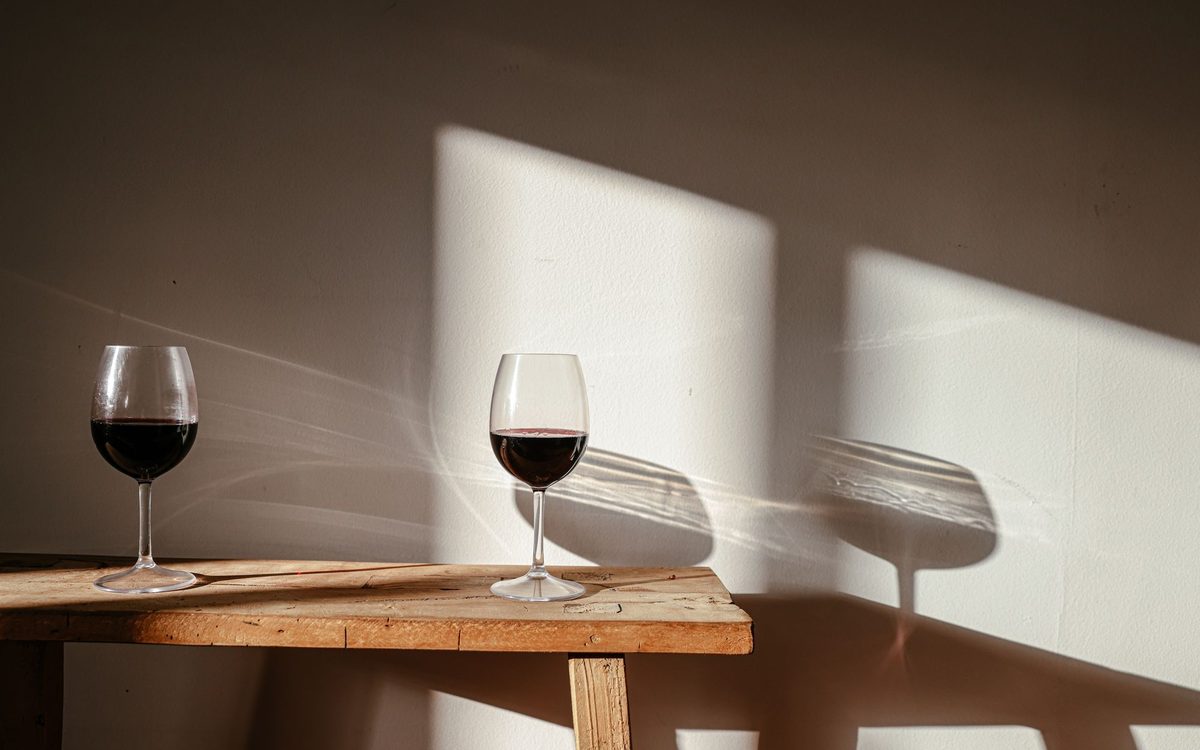 Two glasses of red wine on a wooden bench against a sunlit wall