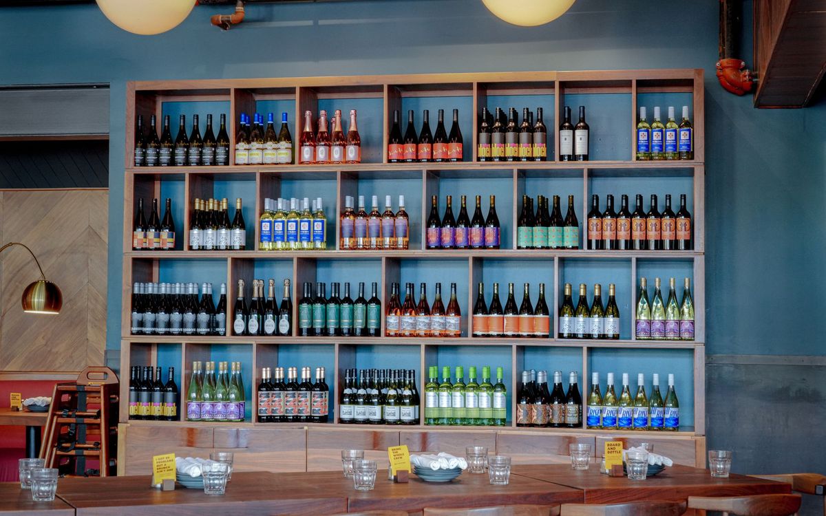 Open wooden shelving filled with rows of wine bottles on a blue wall in a restaurant, an example of a bottle collection on display.