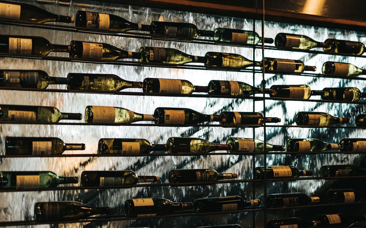 Wine bottles lying on their sides on thin metal racks in front of a textured glass wall, the way bottles are stored horizontally.