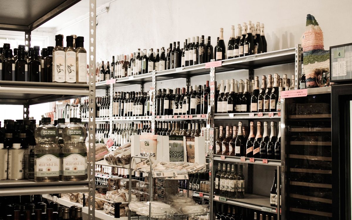 Wine bottles on shop shelves beside a wine fridge, showing the difference between room storage and a dedicated wine fridge.